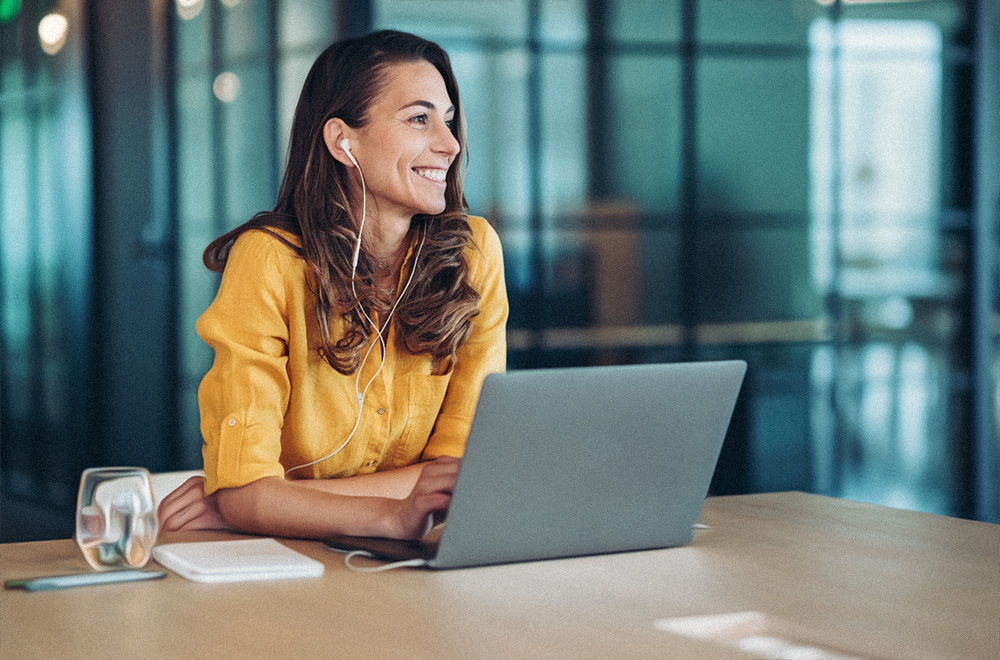 ontspannen en glimlachende kantoormedewerkster achter haar PC dankzij de IT-diensten van het Belgische bedrijf Saphico